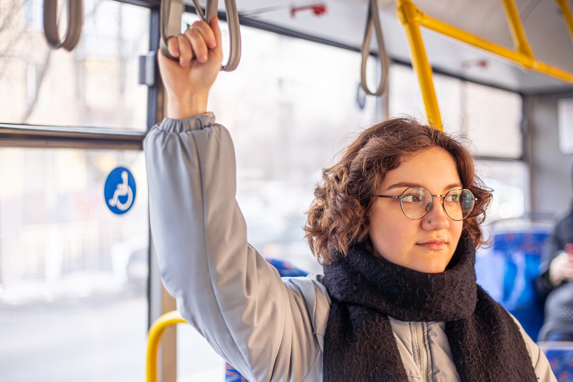 Młoda kobieta w okularach trzyma się uchwytu w autobusie komunikacji miejskiej