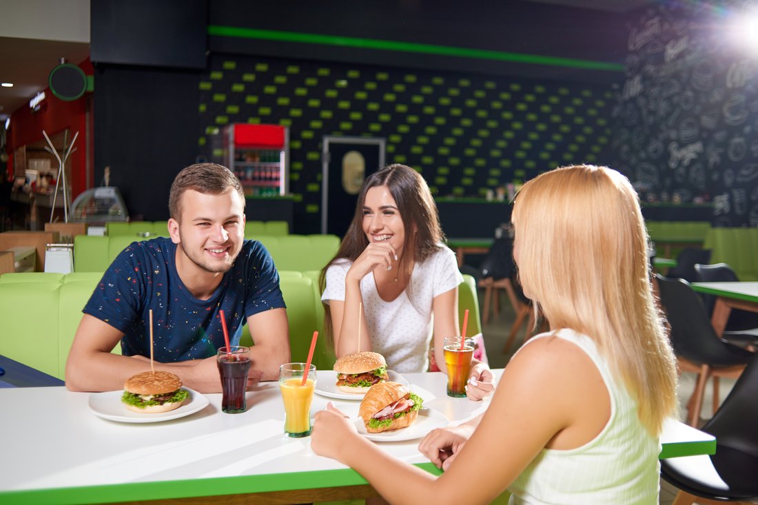 Znajomi śmieją się przy stoliku w kawiarni nad burgerami i napojami