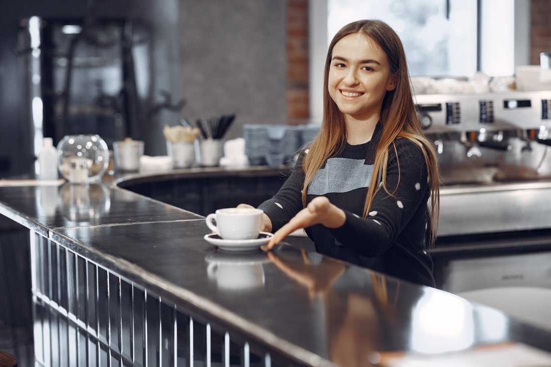 Uśmiechnięta młoda baristka podaje kawę przy ladzie w kawiarni